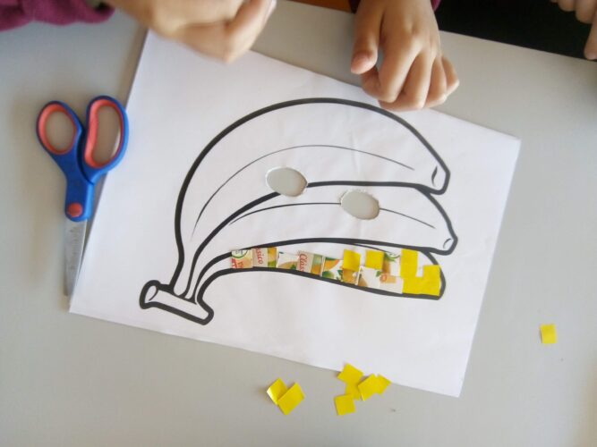 Fase de construção das máscaras<br/>Os alunos colaram os quadradinhos de acordo com as respetivas cores dos frutos, na máscara.